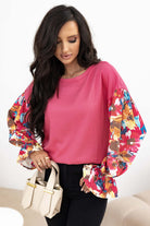 Woman wearing Petal Perfection knit top with colorful ruffled sleeves and a chic patchwork design, holding a handbag.