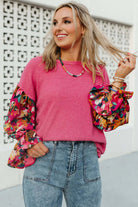 Stylish woman in a pink Petal Perfection knit top with colorful ruffled sleeves and jeans, smiling outdoors.