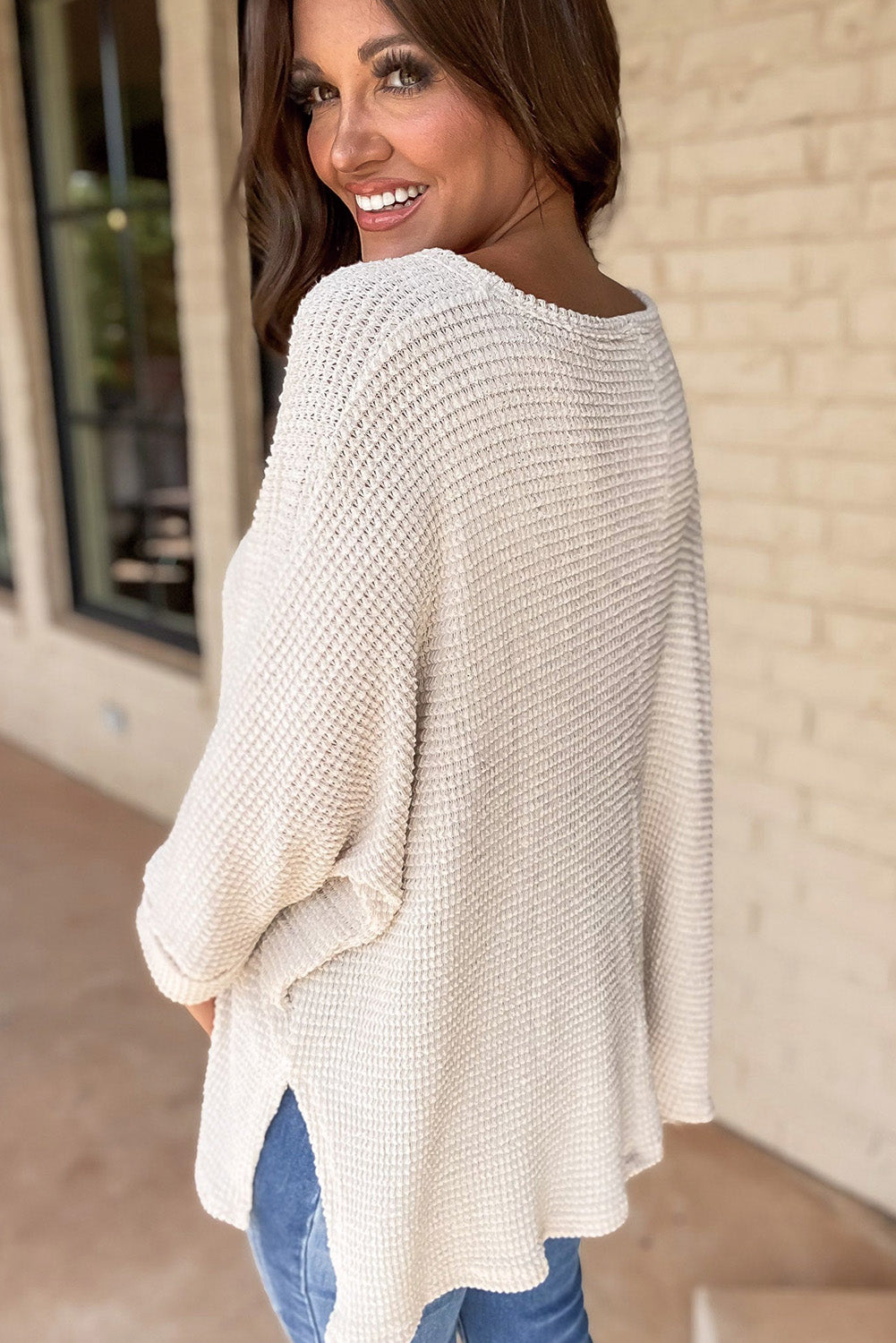 Woman wearing vanilla waffle knit top with side slits and classic loose fit indoors