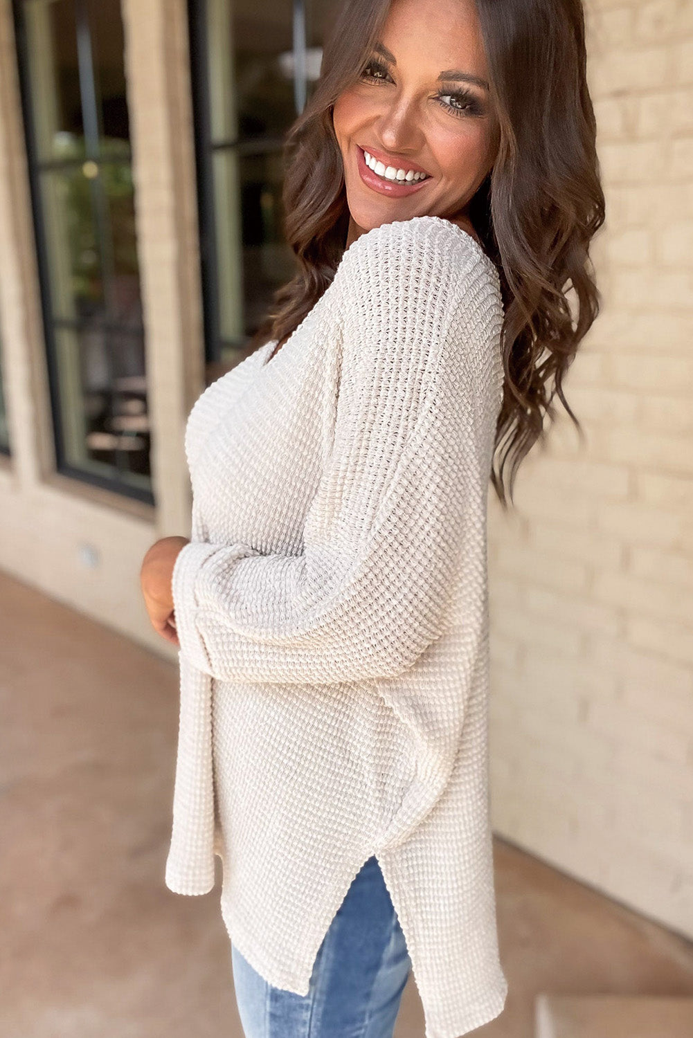 Woman wearing a vanilla waffle knit top with side slits and V-neckline, showcasing the textured design in an outdoor setting.