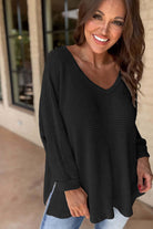 Woman wearing a black Finally Made It top in soft waffle knit, featuring a V-neckline and side slits, smiling outdoors.