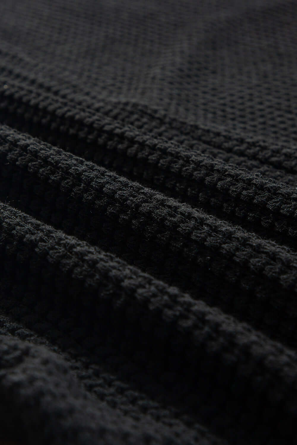 Close-up of black waffle knit fabric showcasing its soft texture and unique design. Perfect for stylish apparel.