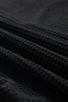 Close-up of black waffle knit fabric showcasing its soft texture and unique design. Perfect for stylish apparel.