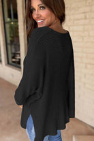 Woman smiling in a black waffle knit top with a loose fit and side slits, showcasing a stylish and comfortable look.