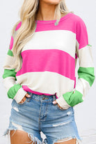 Woman wearing a fuchsia and green color block striped top with long sleeves paired with ripped denim shorts, showcasing a chic casual look.