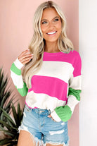 Woman wearing a fuchsia and green striped top with long sleeves and distressed denim shorts, styled for a chic and casual look.