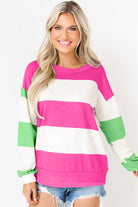 Woman wearing a fuchsia and green striped top with long sleeves and drop shoulder design, paired with denim shorts.