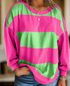 Woman wearing pink and green colorblock crew neck top with drop shoulders and striped pattern, accessorized with layered necklaces.