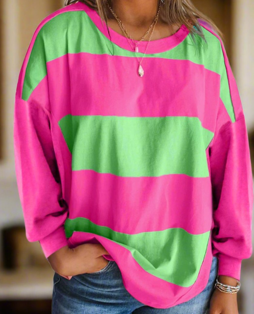 Woman wearing pink and green colorblock crew neck top with drop shoulders and striped pattern, accessorized with layered necklaces.