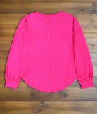 Pink crew neck top with drop shoulder design and vibrant colorblock pattern on wooden background