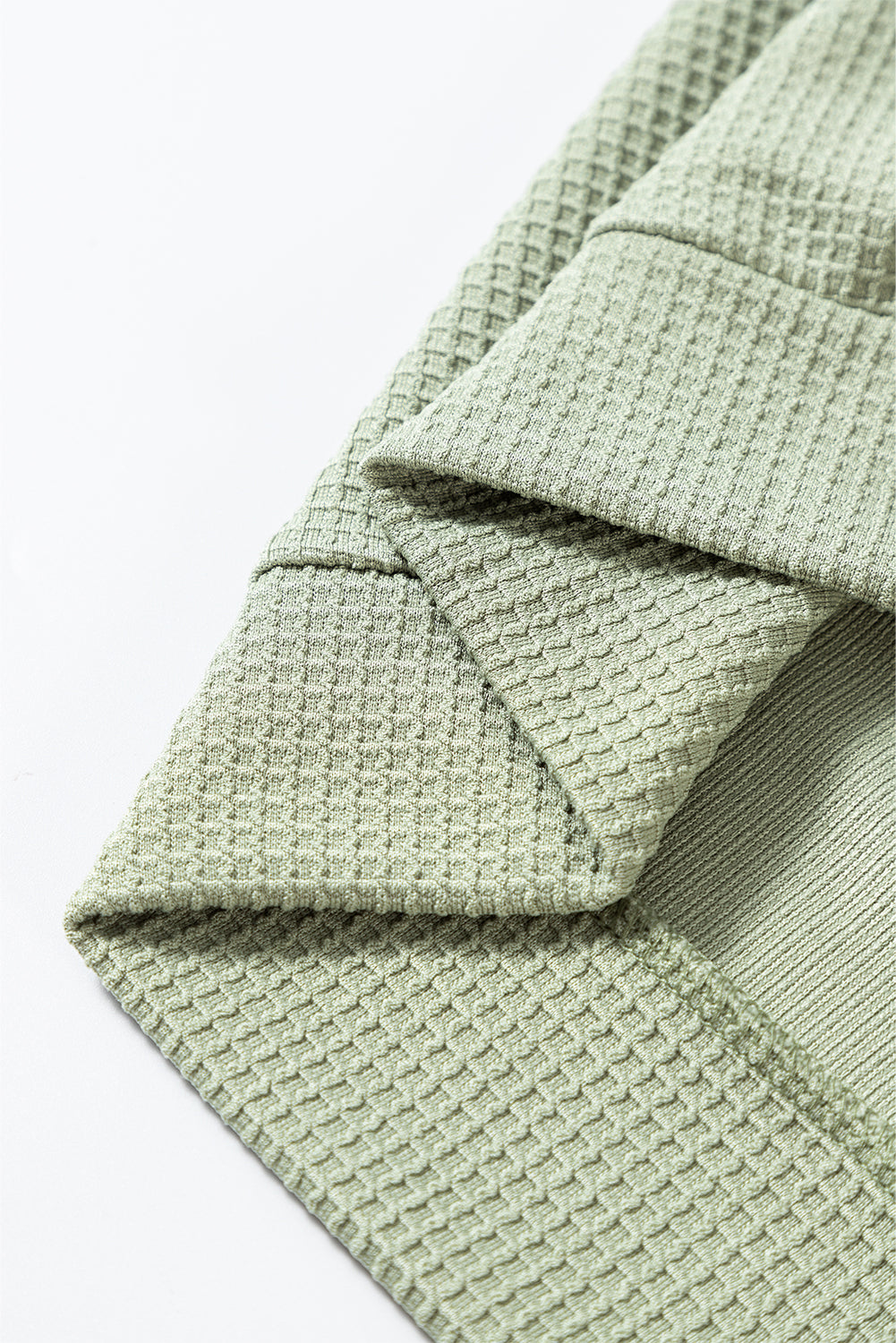 Close-up of green waffle knit fabric showcasing stylish texture and detailed stitching on a fashionable t-shirt.