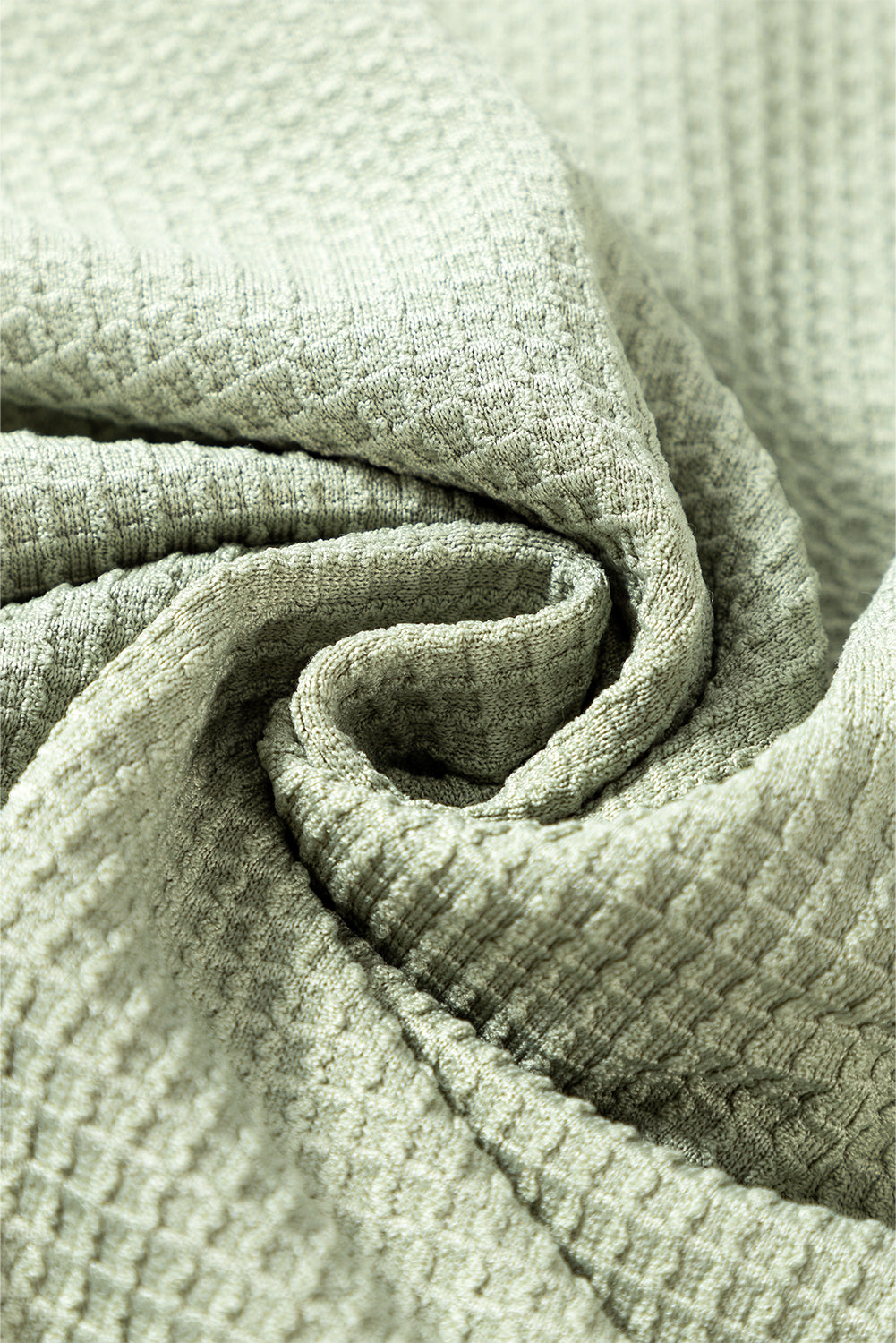 Close-up of misty green waffle knit fabric texture with intricate details.