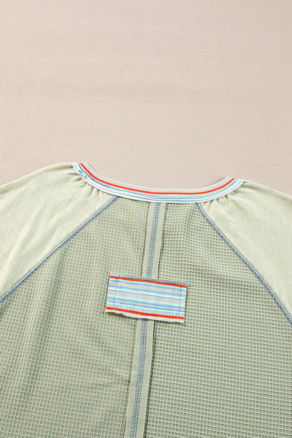 Stylish waffle knit t-shirt with raglan sleeves, patchwork design, and contrasting stripe detail on beige background.