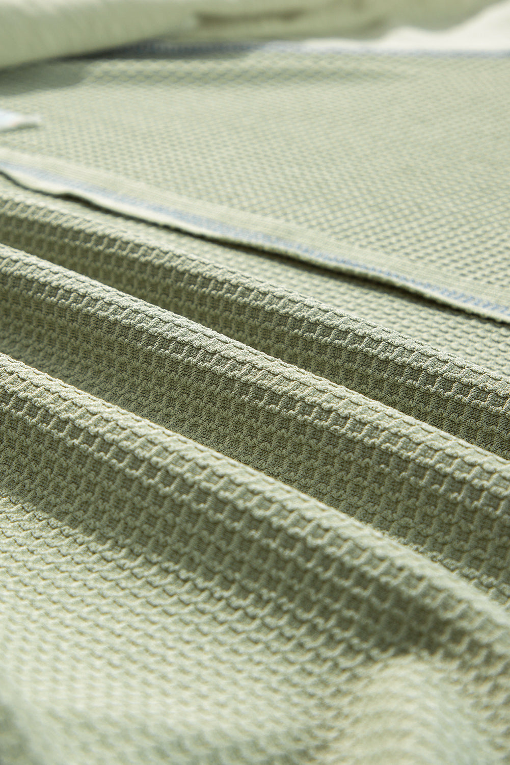 Close-up of green waffle knit fabric showing textured pattern and stitching detail of MIST OVER THE MEADOW t-shirt.