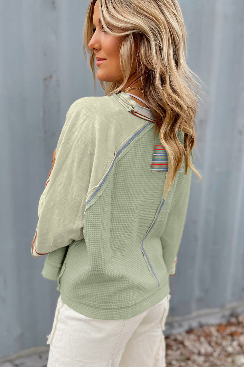 Woman wearing a stylish waffle knit t-shirt with patchwork design, wide bracelet sleeves, and raw hem, paired with white pants.