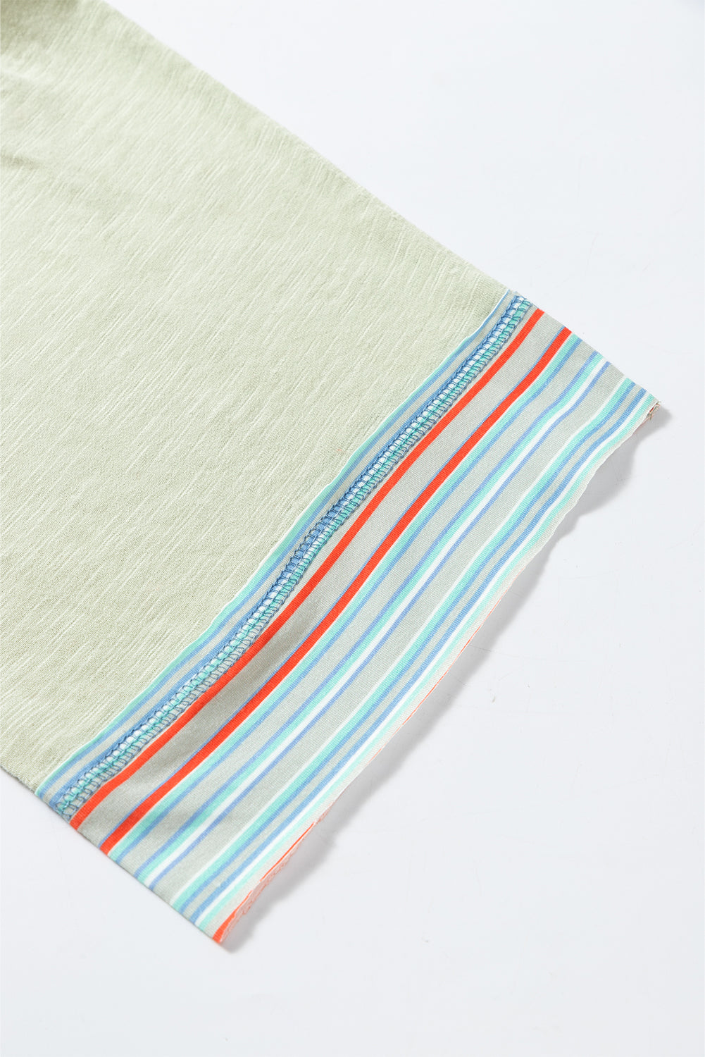 Close-up of a t-shirt sleeve with contrast stripe stitching on a waffle knit fabric, featuring pastel colors and raw hem finish.