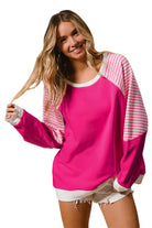 Woman smiling in a pink and striped patchwork crew neck top by Vivian-Lu, featuring sporty raglan sleeves and a loose fit.