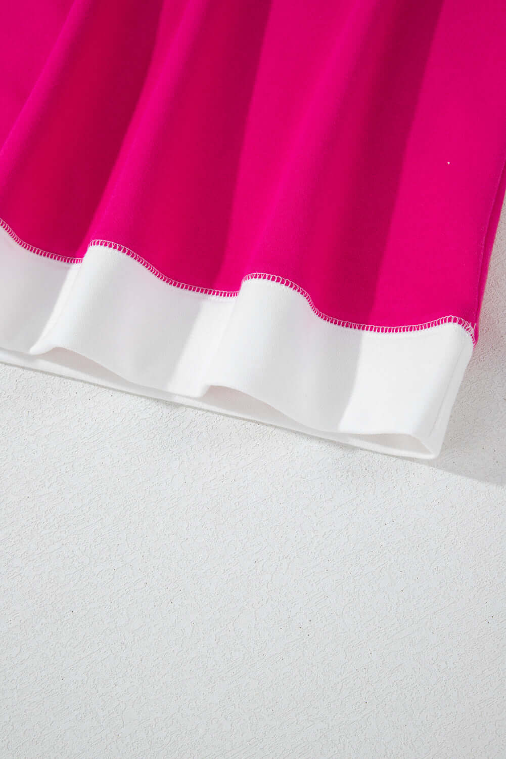 Close-up of the vibrant pink hem of the PROMISE YOU Top by Vivian-Lu, showcasing its stylish contrast with white trim.