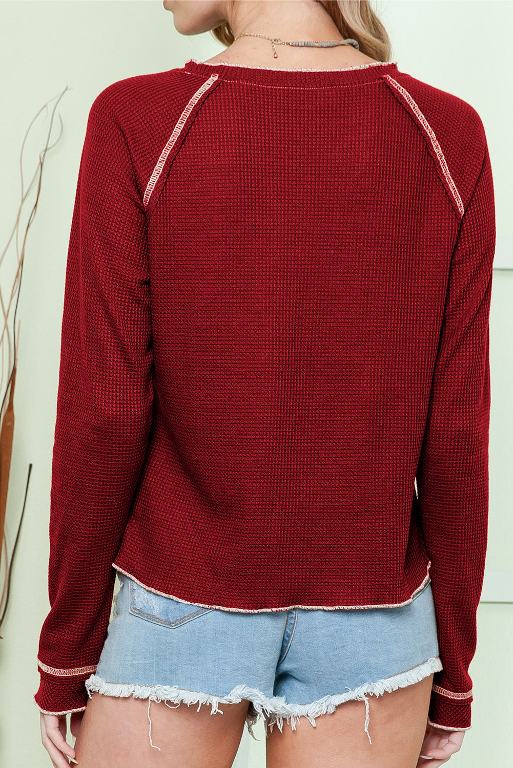 Woman wearing a maroon waffle knit KICKOFF TIME TOP with raglan sleeves, paired with denim shorts, viewed from the back.