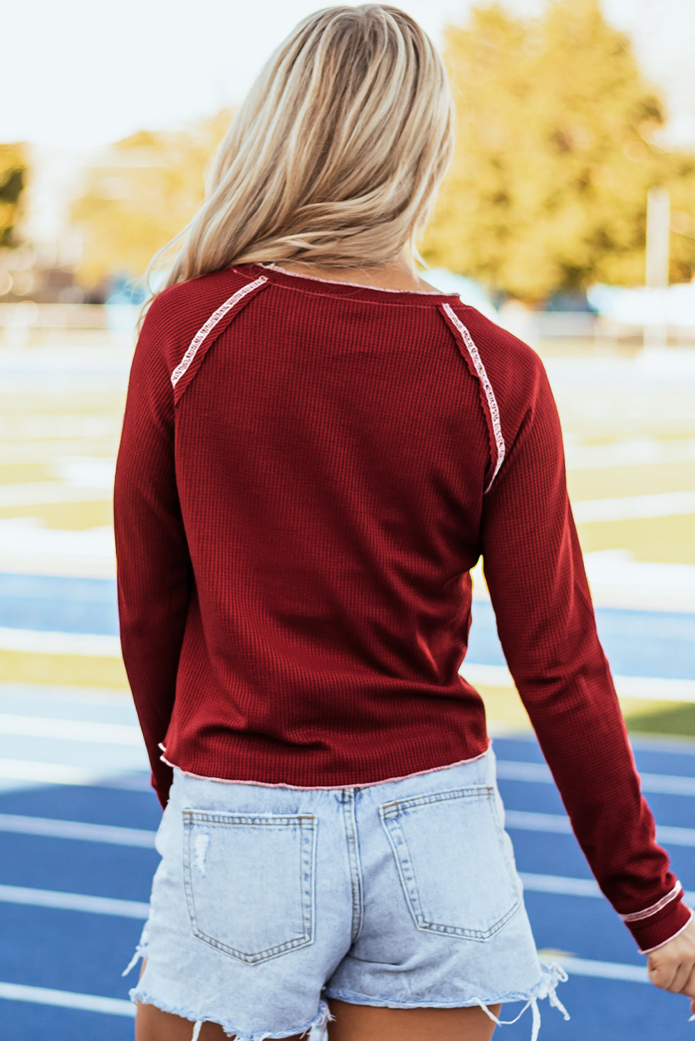 Woman wearing a Kickoff Time Top with raglan sleeves and red waffle knit fabric, standing on a sports track.