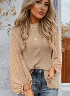 Woman wearing beige balloon sleeve blouse with Swiss dot pattern, paired with jeans. Sophisticated autumn fashion outdoor style.