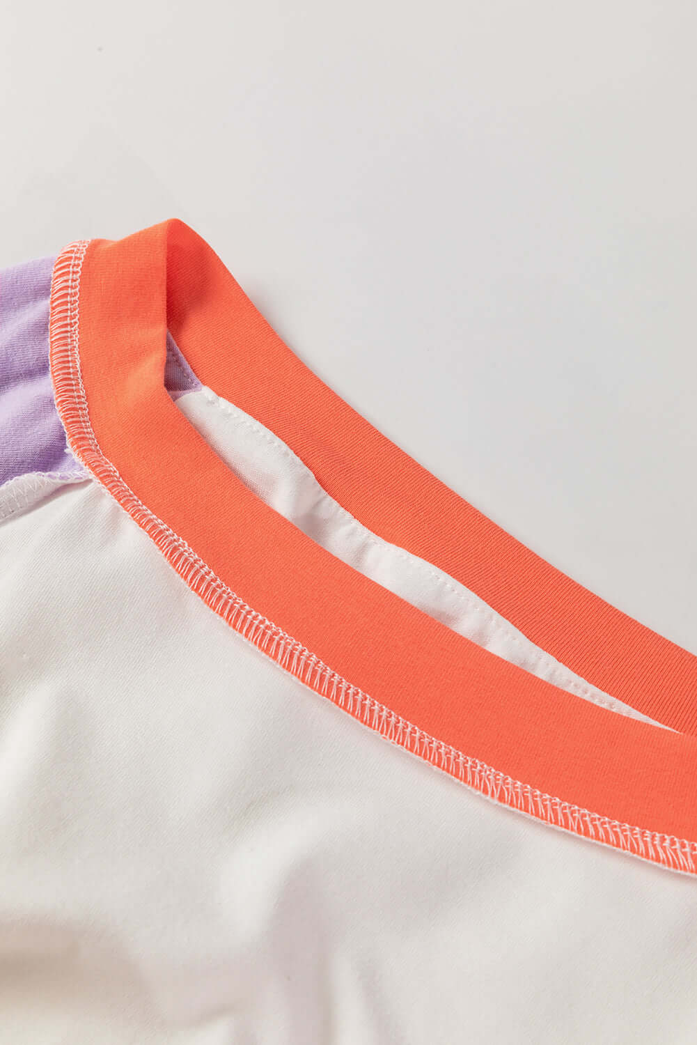 Close-up of Enchanted Aura Top showcasing chic orange and purple color-block neckline detail.