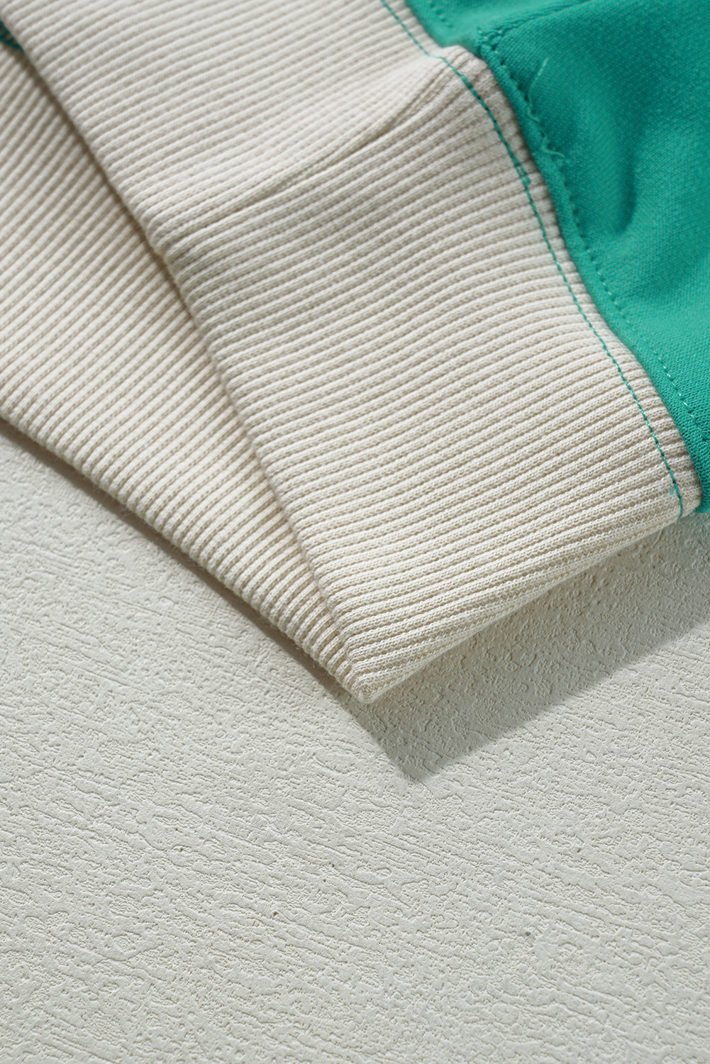 Close-up of teal green Malibu Marina top sleeve with ribbed cream cuff and contrasting color block design.