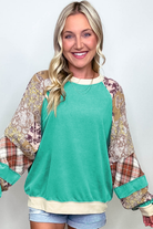 Woman wearing teal green Malibu Marina top with plaid and paisley patterned sleeves, showcasing a chic raglan patchwork design.