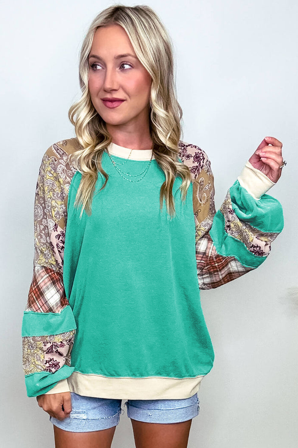 Woman wearing Malibu Marina top in teal with plaid and paisley sleeves, showcasing unique raglan patchwork and color block design.