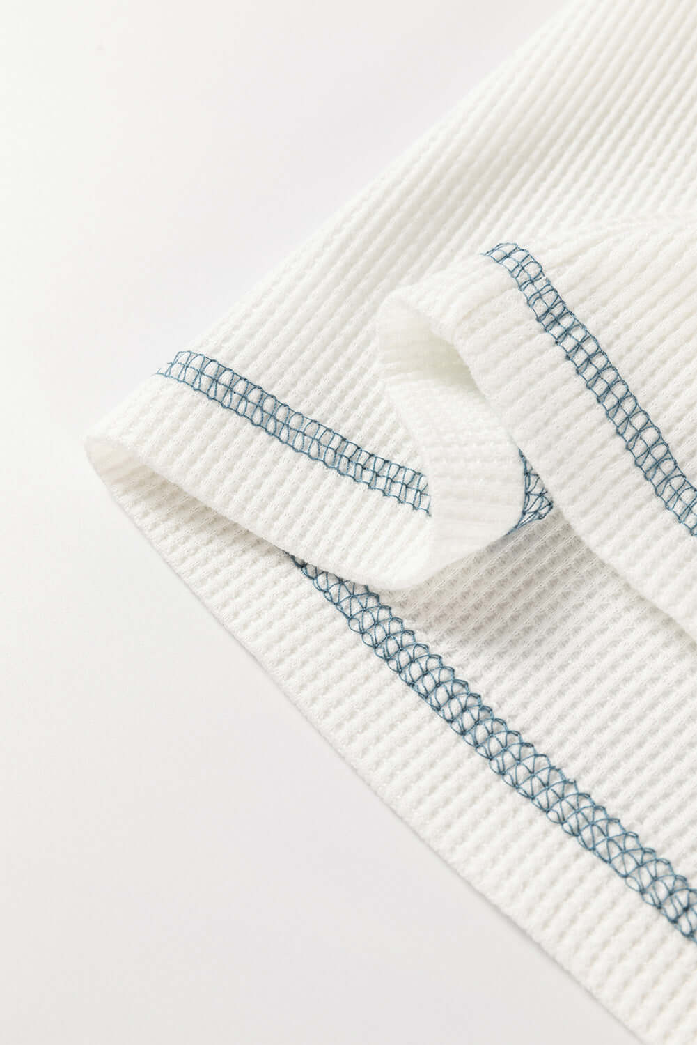 Textured white fabric with blue stitching detail, showcasing a boho-inspired design for casual wear.