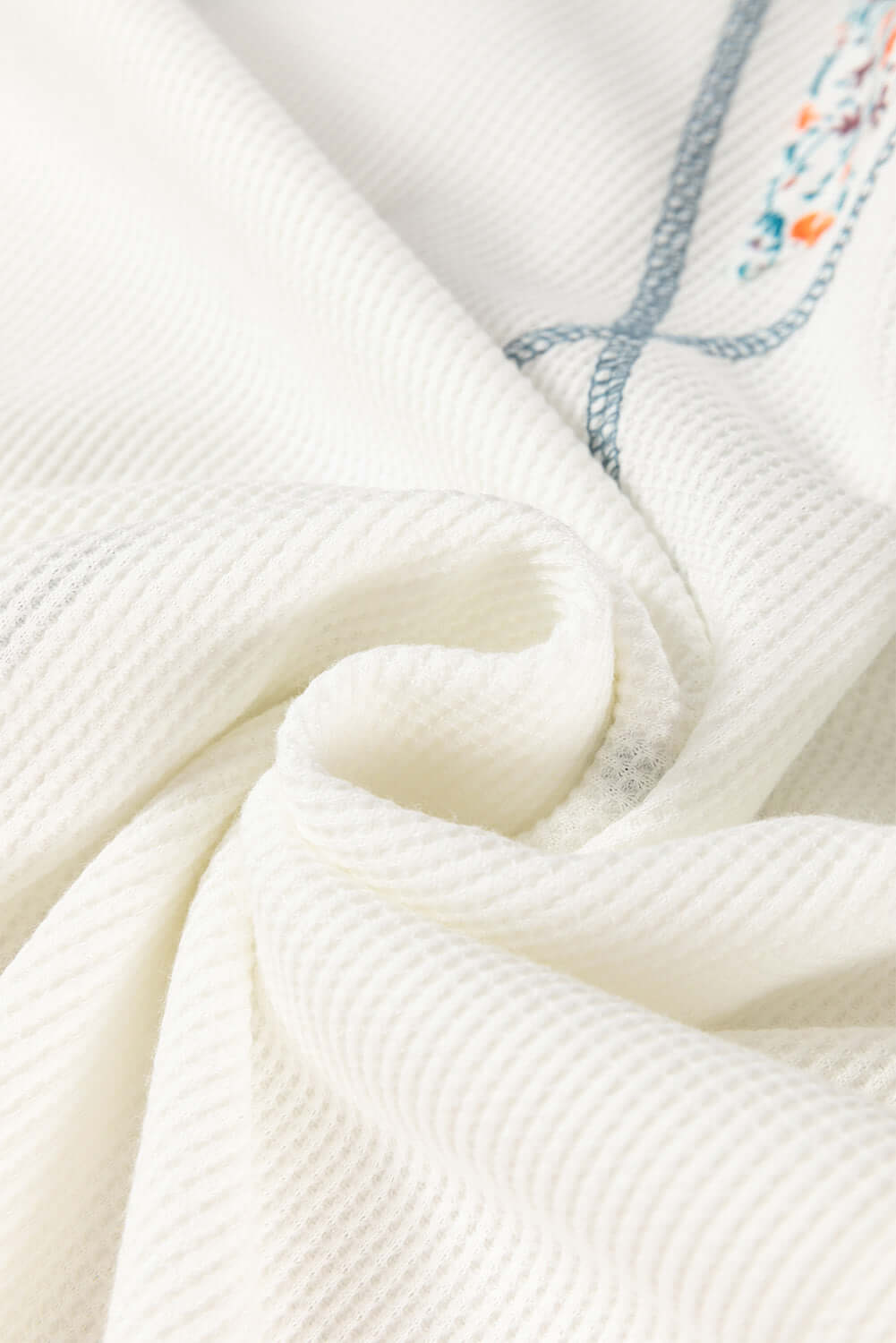 Close-up of textured white waffle knit fabric showcasing floral embroidery details for the Serene Skies Top.