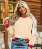 Woman wearing Ties That Bind crewneck top with ribbon bows on sleeves and vibrant red trim, styled with denim.