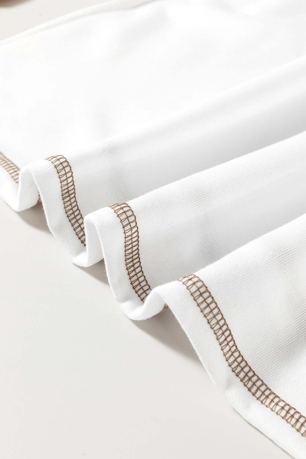 Close-up of the Fine Line Top's white fabric with tan patchwork and stylish striped accents.