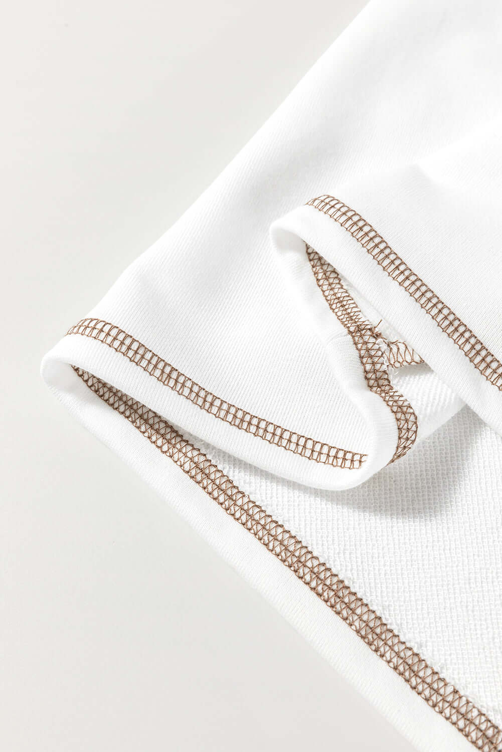 Close-up of A Fine Line Top's white fabric with tan stitched detailing and folded sleeve for a stylish look.