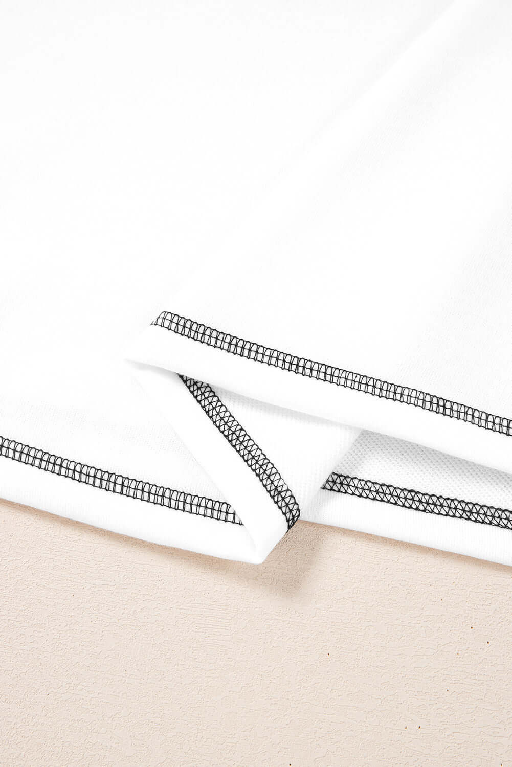 Close-up of A Fine Line Top's white fabric with black trim, highlighting patchwork design and stylish sleeves.