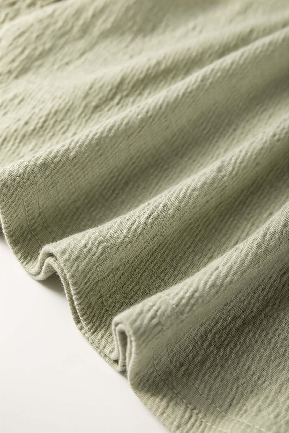 Close-up of textured mint sage fabric, showcasing its intricate weave and soft drape, perfect for stylish clothing.