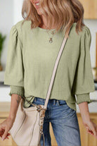 Woman in minty sage ALPINE MIST top with half sleeves, styled with denim and a chic bag, exuding a trendy casual look.