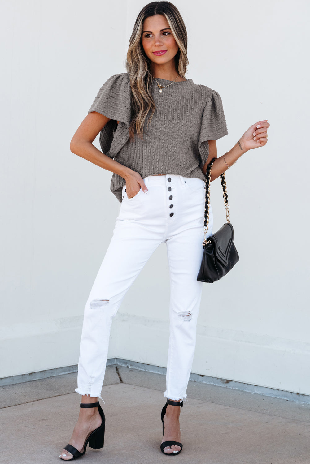 Chic woman in a textured ruffle sleeve taupe-gray top and white jeans, stylishly accessorized.