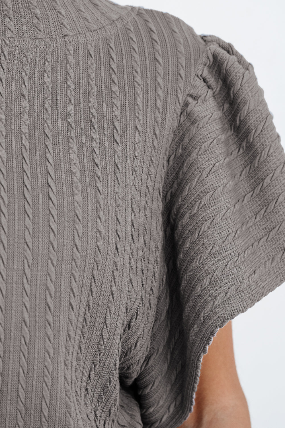 Close-up of textured taupe-gray ruffle sleeve top featuring cable-knit design, perfect for stylish layering.