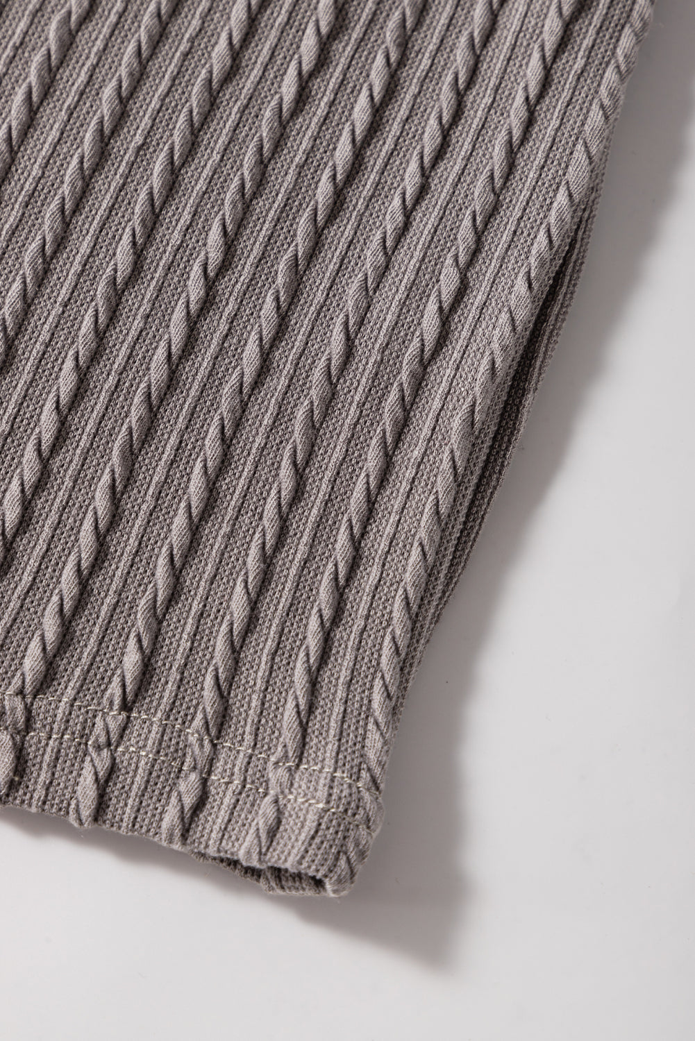 Textured taupe-gray fabric showcasing cable-knit design, ideal for chic fashion styling with ruffle sleeves.