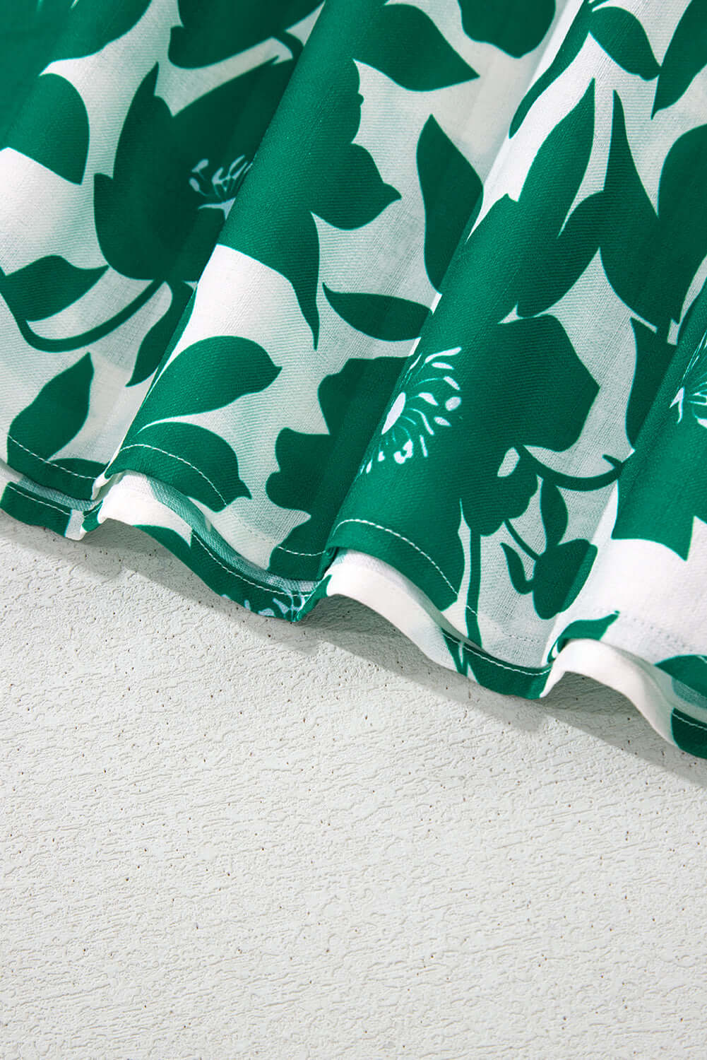 Close-up of the floral print and ruffled edge of the Jade Blooms Top in green and white.