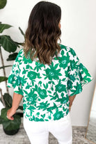 Woman wearing Jade Blooms Top with green floral print and ruffled sleeves, showcasing a casual yet elegant style.