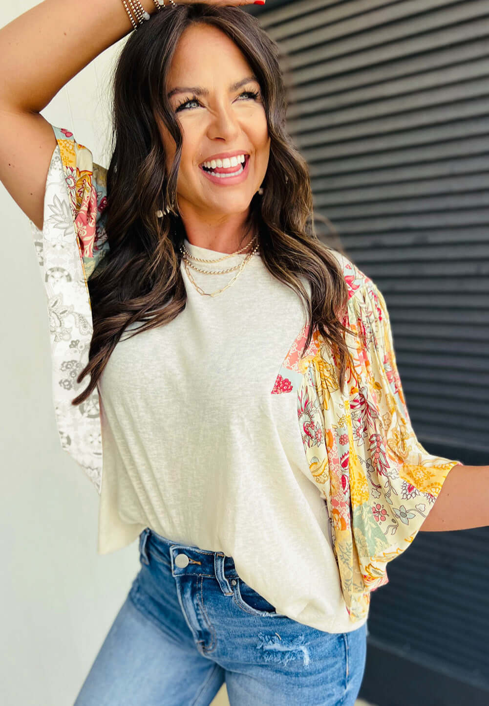 Woman smiling in a stylish Sun Dance top with floral prints and half batwing sleeves, paired with jeans.