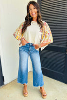 Model wearing Sun Dance top with floral prints, paired with trendy jeans and wedges, showcasing a bohemian style.