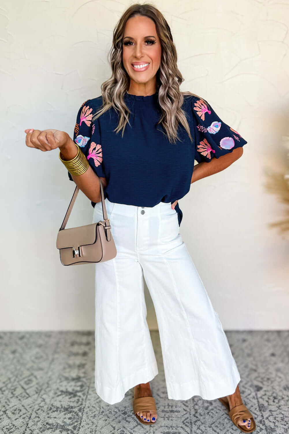 Model wearing Tide and Treasure Blouse with seashell embroidery, paired with white wide-leg pants.