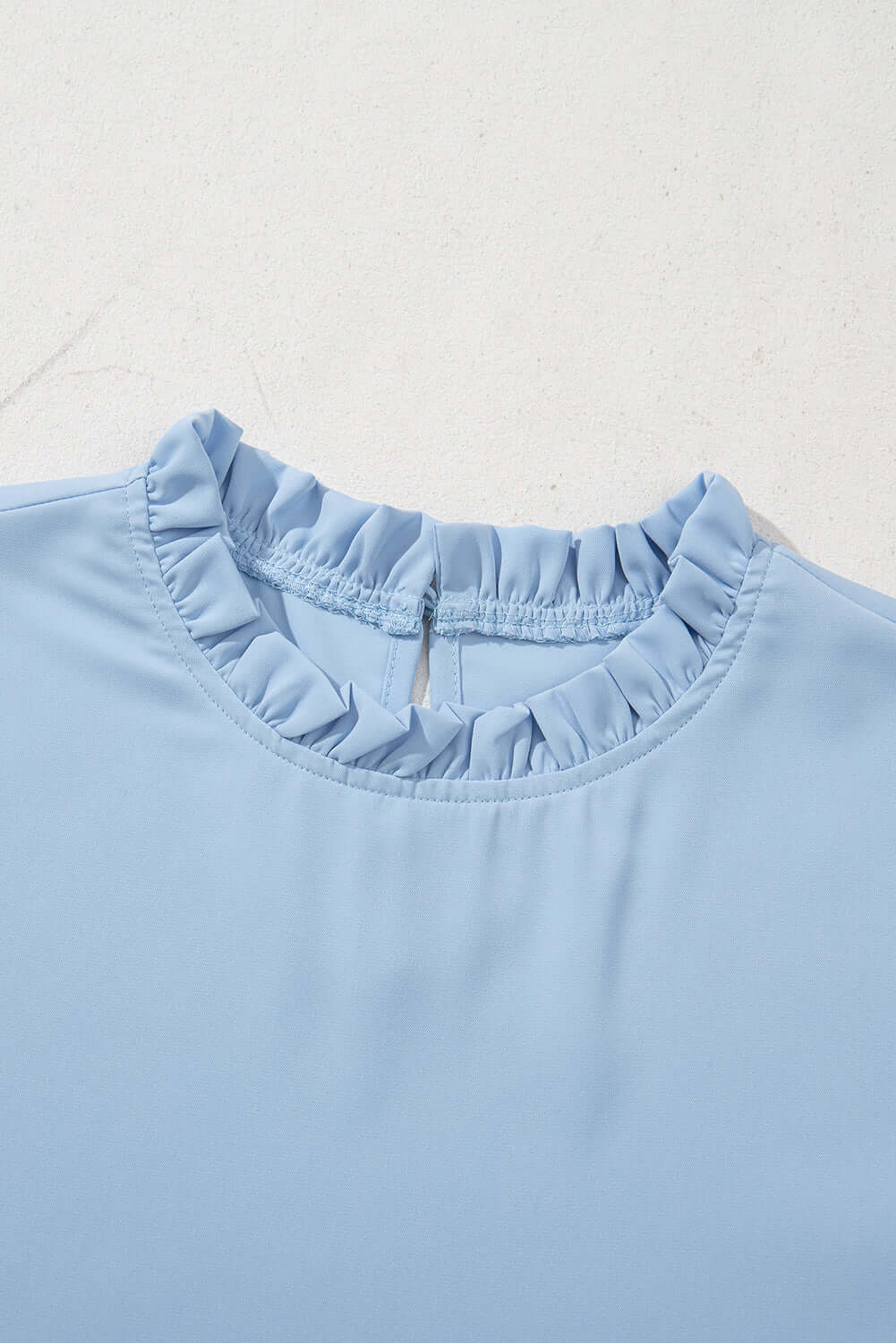 Close-up of light blue Frill Seeker Top showcasing ruffle trim at the neckline for a chic and feminine look.