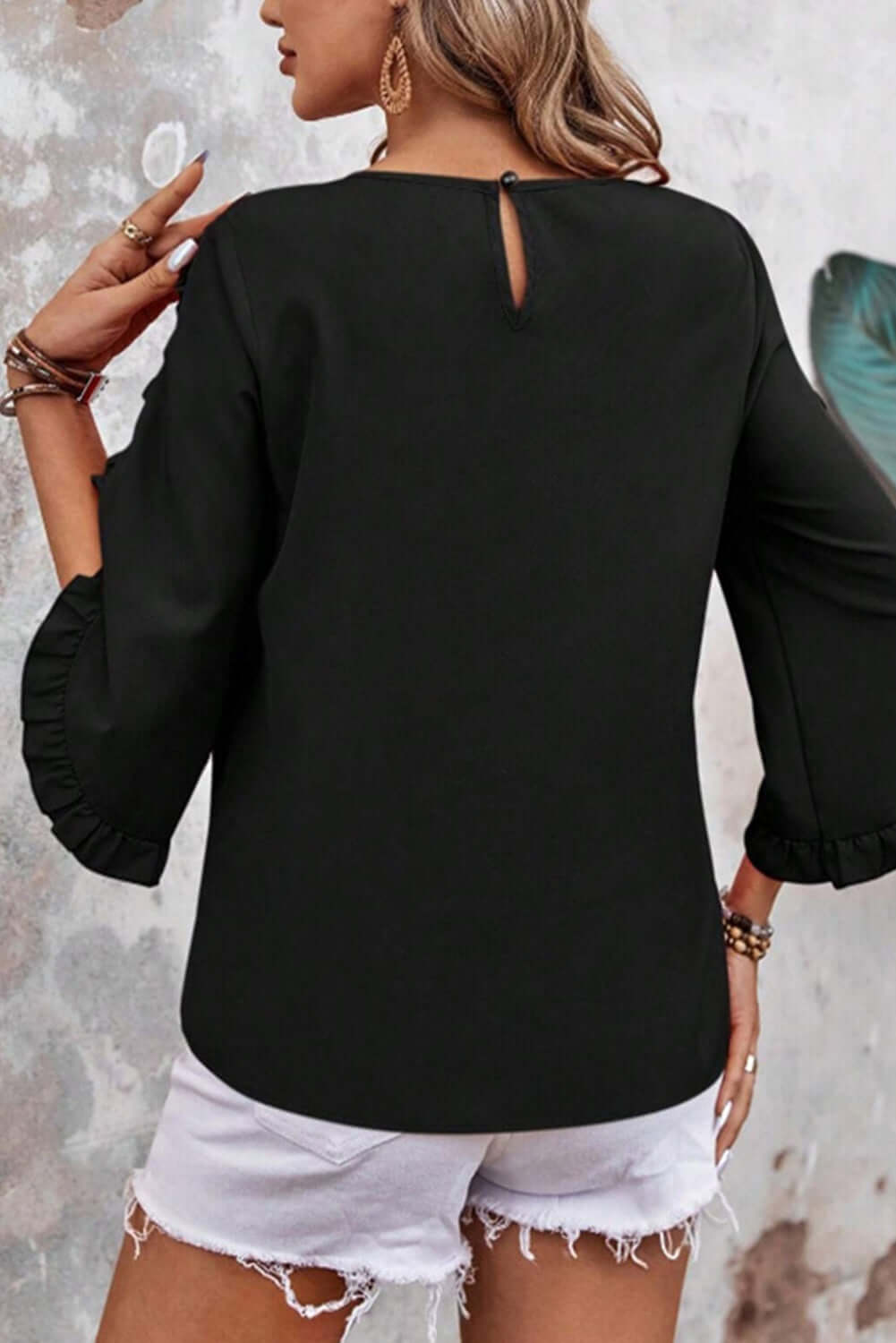 Back view of a black ruffle sleeve blouse paired with white shorts, showcasing elegant design and relaxed fit.