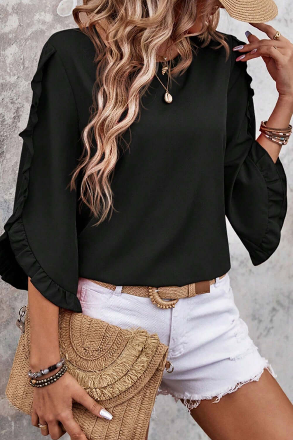 Fringe Benefits black ruffle sleeve blouse styled with white shorts and a straw bag, showcasing chic summer fashion.