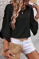 Fringe Benefits black ruffle sleeve blouse styled with white shorts and a straw bag, showcasing chic summer fashion.