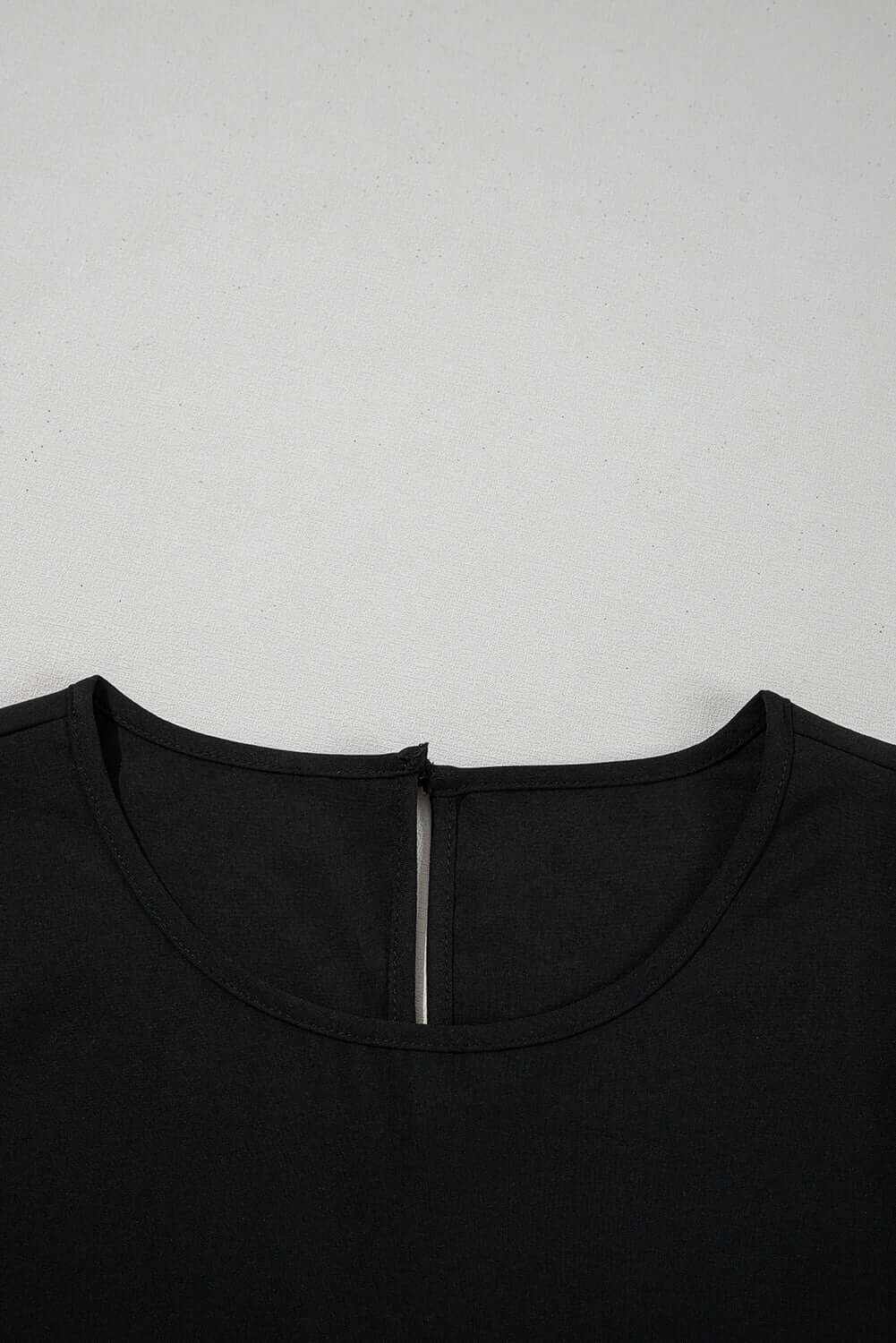 Close-up of the round neck of the Fringe Benefits black blouse featuring a back zipper detail.
